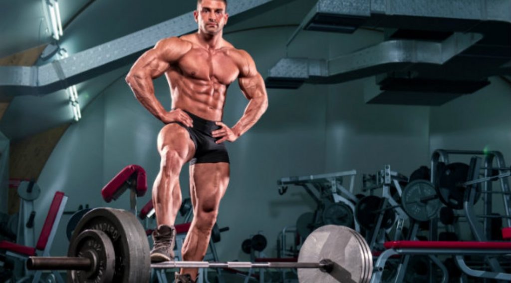 a bodybuilder standing by a deadlift bar