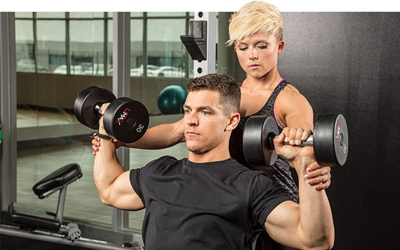 a woman spotting a man with dumbbell shoulder presses