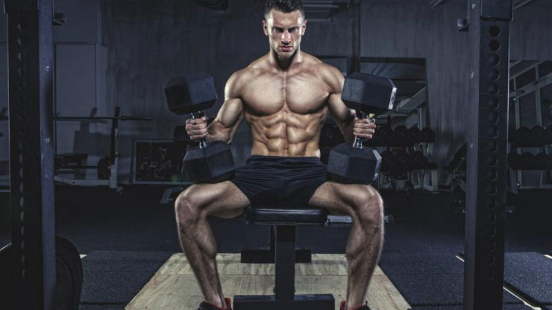 Muscular athlete getting ready for a dumbbell bench press on dark background