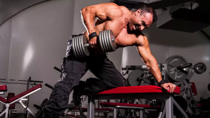 Muscular bodybuilder performing single arm row in the gym