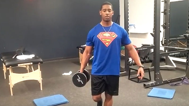 Male athlete performs unilateral loaded carries with a dumbbell in the gym
