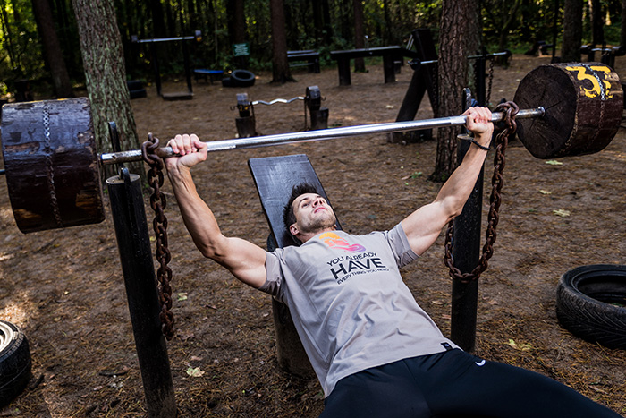 man doing bench press outside with homemade weights 