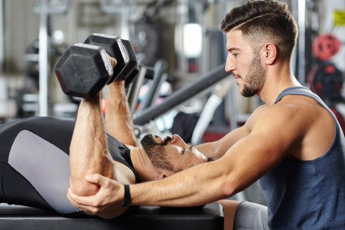 personal trainer instructing client in dumbbell press