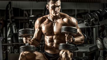 bodybuilder performing muscle building program with two dumbbells
