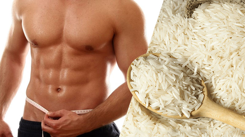 Ripped athlete measuring waist with tape measure, standing next to white rice