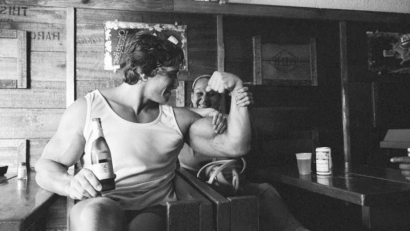 Arnold Schwarzenegger drinking bottle of beer to show how bodybuilders drink alcohol on occassion