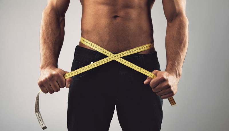 Low body fat percentage man holding tape measure against waist